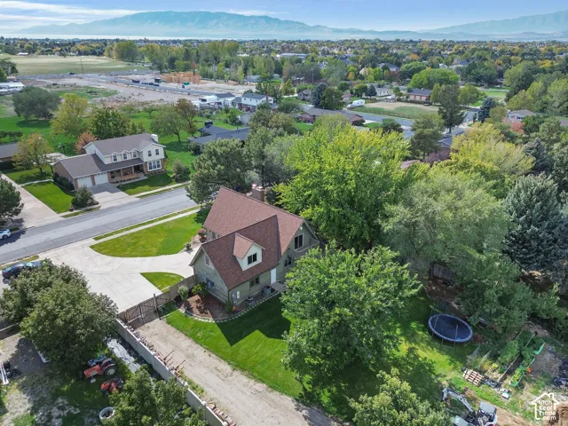 Aerial perspective featuring a multi-level residence with a gable roof, paved driveway, mature trees, manicured lawn, and mountain backdrop