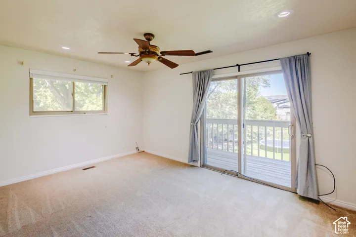 Carpeted room featuring a ceiling fan with integrated light fixture, recessed lighting, slider door access to an exterior deck, and large picture window