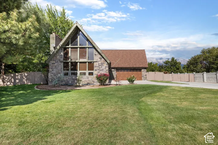 A-frame exterior featuring stone masonry, expansive floor-to-ceiling windows, attached garage, and manicured lawn