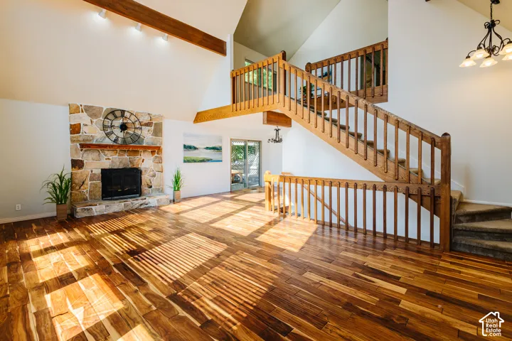 Vaulted ceilings with exposed timber beams, stone-faced fireplace, wood-finish flooring, and wooden staircase featuring decorative railings