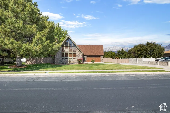 A-frame residence featuring stone exterior siding, floor-to-ceiling windows, attached garage, and mountain backdrop
