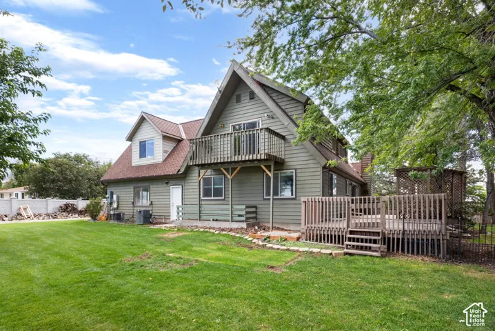 Multi-story residence featuring lap siding, an elevated wood balcony, a ground-level wood deck, and expansive lawn area