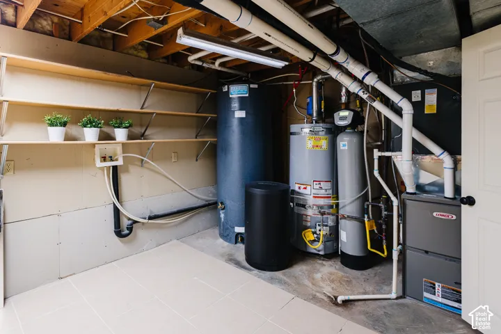 Utility area featuring tile flooring, built-in wall shelving, a water heater, a water softener system, and a gas-fired furnace