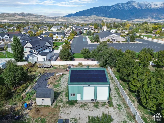 Detached metal-sided structure featuring dual garage bays, roof-mounted solar panels, a cupola, and a secondary storage shed, set against a mountainous backdrop