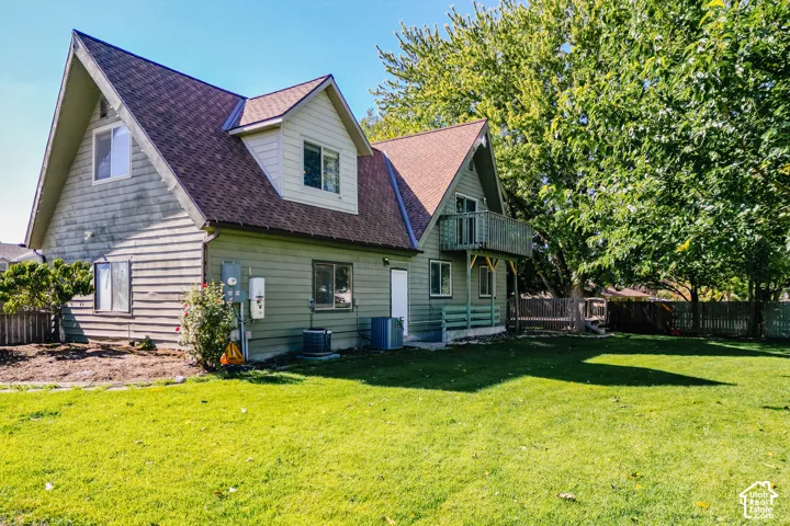 A-frame style exterior featuring horizontal lap siding, a shingled roof, a second-story balcony, and a fenced backyard with mature trees