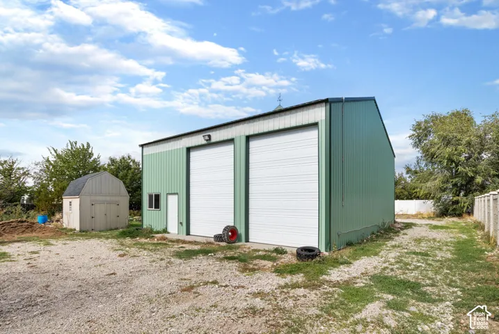 Detached metal-sided workshop featuring two roll-up garage doors, a pedestrian door, a cupola, and an additional storage shed