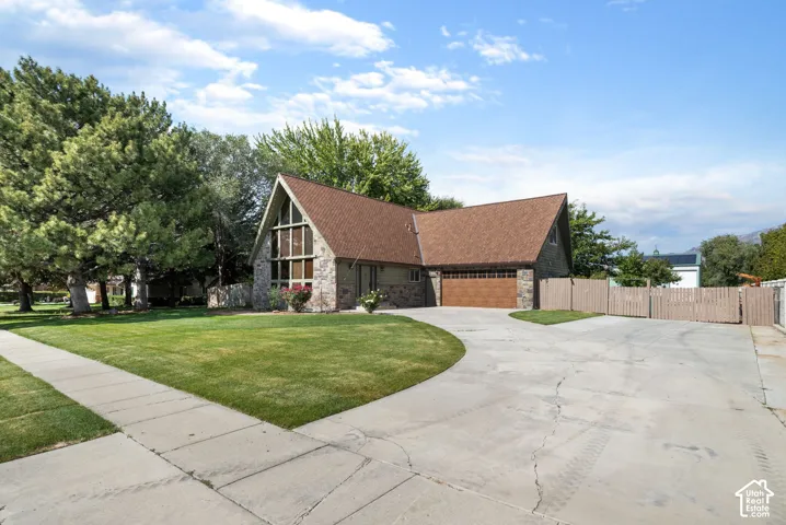 A-frame architectural exterior featuring stone facade accents, expansive multi-pane windows, asphalt shingle roofing, and an attached multi-car garage with wood-finish door