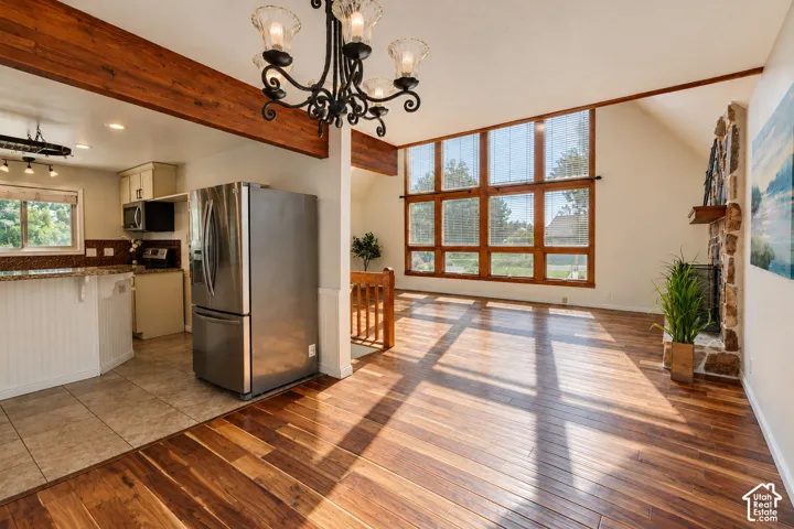 Open floor plan featuring wood-finish flooring, vaulted ceilings with exposed wood beams, a floor-to-ceiling stone fireplace, and expansive multi-pane windows
