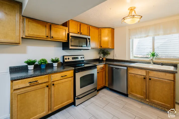 Kitchen featuring shaker-style wood cabinetry, dark stone-finish countertops, stainless steel appliances, a white basin sink, and wood-finish tile flooring