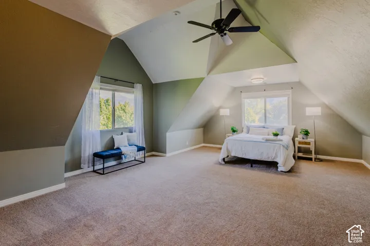 Vaulted ceilings with architectural angles, carpeted flooring, two large windows, and a ceiling fan