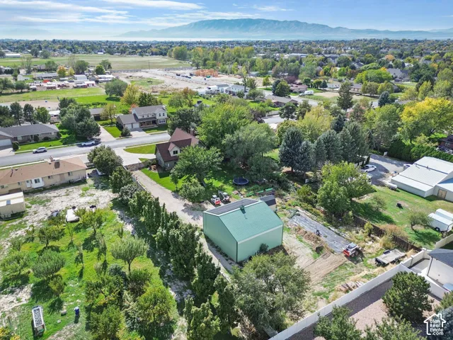 Aerial perspective featuring a metal-sided outbuilding with a pitched roof, mature coniferous and deciduous trees, and mountain backdrop