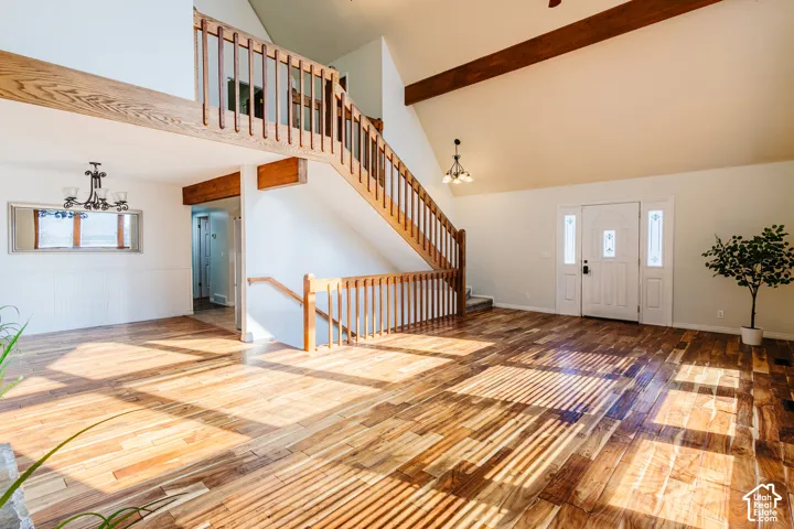 Vaulted ceilings with exposed timber beams, wood-finish flooring, staircase with a wood railing, and an entry door with sidelights