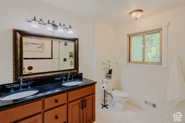 Dual-sink vanity with dark stone countertop, integrated undermount sinks, and traditional wood-finish cabinetry