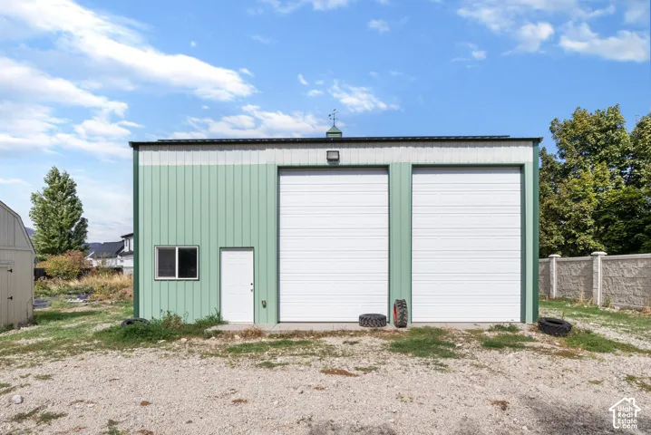 Detached metal workshop featuring two oversized roll-up garage doors, a side-entry pedestrian door, a metal roof, and a cupola
