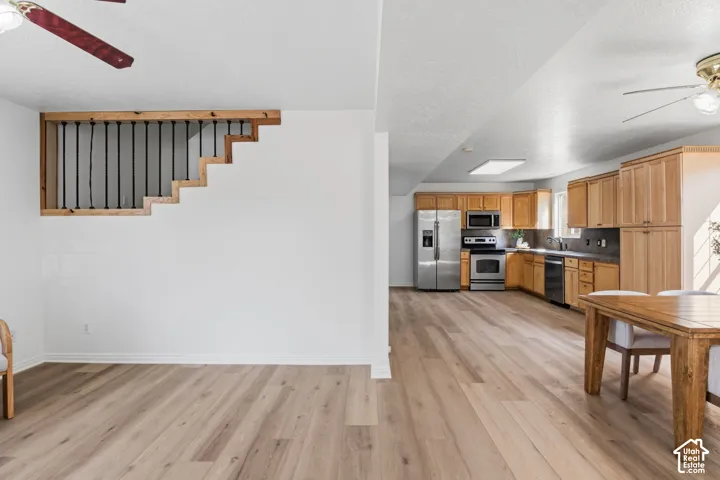 Open-concept interior featuring wood-finish flooring, wood cabinetry, stainless steel appliances, and a staircase railing with black metal balusters