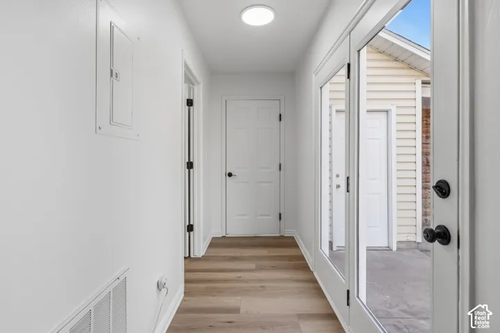 Hallway featuring wood-finish flooring, white paneled doors, flush-mount ceiling lighting, and a glass-paneled entry door opening to an exterior concrete patio