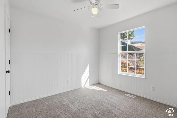 Neutral-toned carpeting, white wainscoting, multi-pane window, and a ceiling fan with integrated lighting