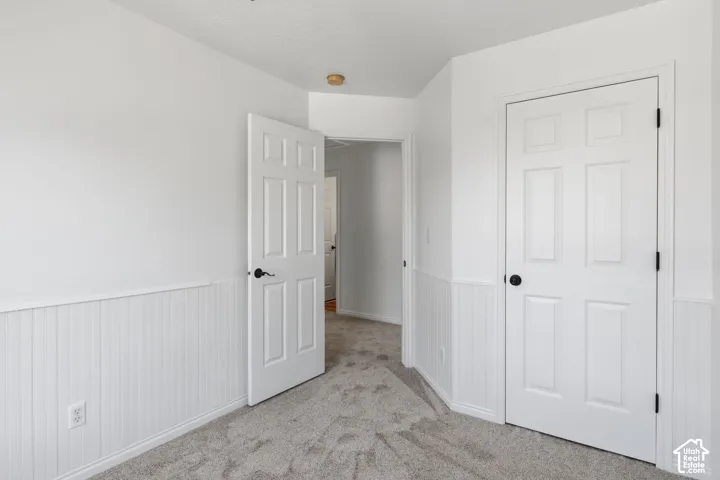 Neutral-toned carpeting, white wainscoting, and six-panel interior doors with matte black hardware
