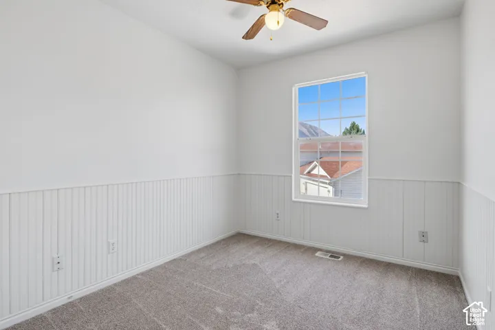 Neutral interior featuring floor-to-ceiling white beadboard wainscoting, neutral carpeting, and a ceiling fan with integrated lighting