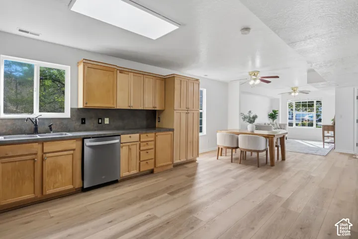 Kitchen featuring wood cabinetry, stainless steel dishwasher, dark-toned backsplash, wood-finish flooring, and two ceiling-mounted fans