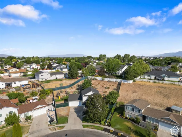 Aerial perspective featuring a multi-level suburban residence with an attached garage, concrete driveway, and a spacious lot with mountain silhouettes in the distance