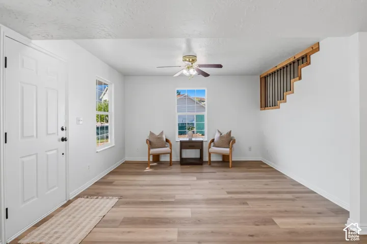 Interior space featuring wood-finish flooring, white walls, a ceiling-mounted light fixture with a fan, and an open wood-slat staircase railing