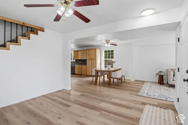 Wood-finish flooring, staircase with a wood handrail and dark metal balusters, wooden cabinetry, and dual ceiling fans