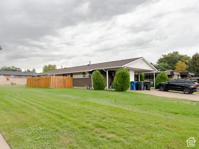 Single-story brick exterior featuring a covered carport, expansive lawn, and wood-panel privacy fencing