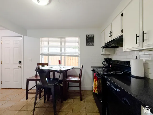 Kitchen featuring white shaker-style cabinetry, black hardware, white subway tile backsplash, dark countertops, and tile flooring