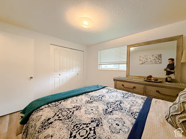 Bedroom featuring wood-finish flooring, dual-panel closet doors, and a window with fitted horizontal blinds