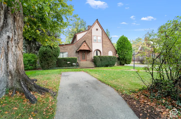 Tudor-style exterior featuring brick and stucco siding, a steeply pitched roofline, decorative arched window, and concrete walkway
