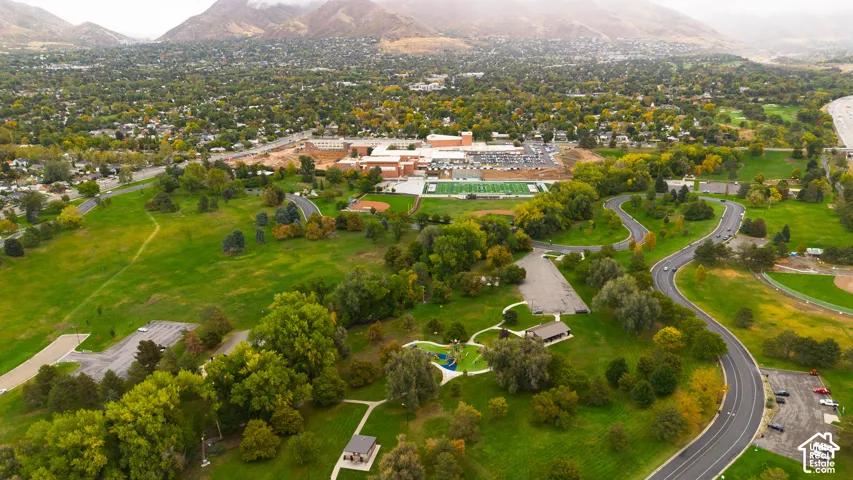 Aerial perspective featuring expansive green space, mature trees, paved walking paths, a public pavilion, and mountain backdrop