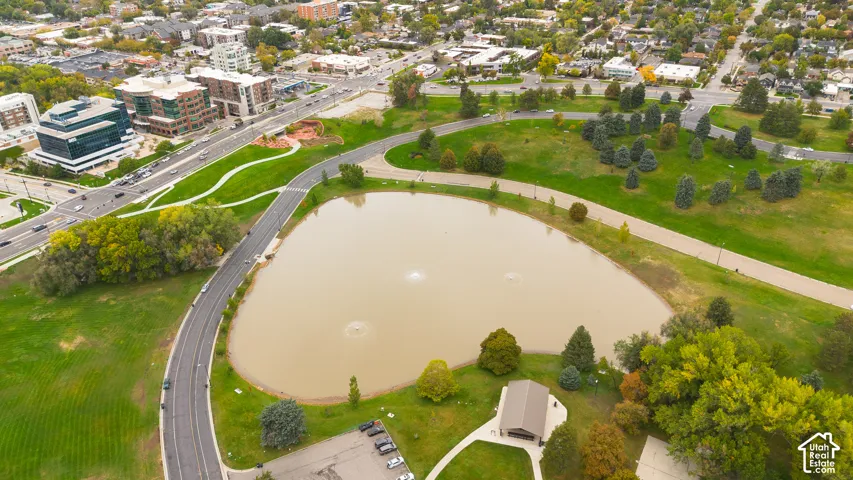 Aerial perspective of a pond with integrated water fountains, expansive grass-covered grounds, paved walking paths, and a structure with a pitched roof