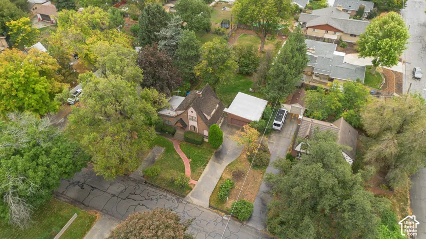 Aerial view of a multi-story residence with a pitched roof, featuring a detached garage, concrete driveway, and brick walkway set amidst mature trees and landscaping