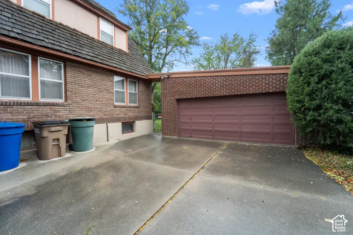 Exterior featuring a brick facade, cedar shake roofing, and a two-car attached garage with a paved driveway