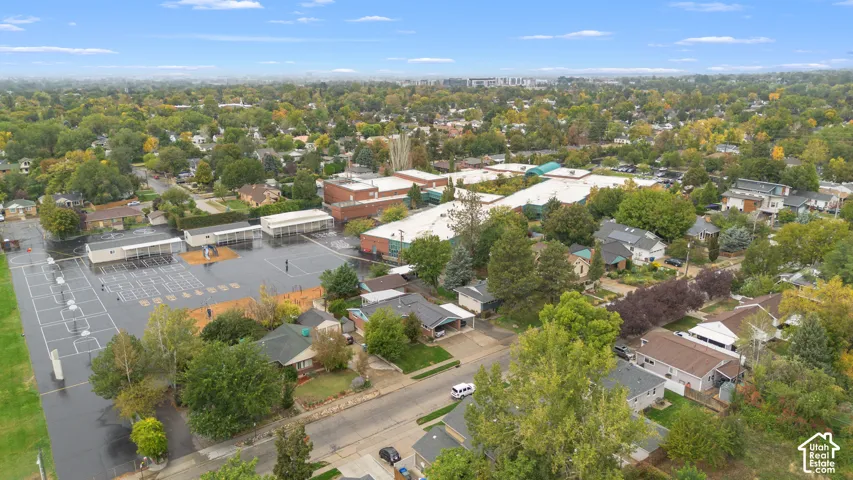 Aerial perspective of a suburban neighborhood featuring mature canopy trees, asphalt roadways, varied residential rooflines, and paved surface lots