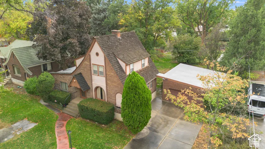 Brick exterior featuring a steeply pitched roof, arched entryway, and detached garage with a concrete driveway, surrounded by mature trees