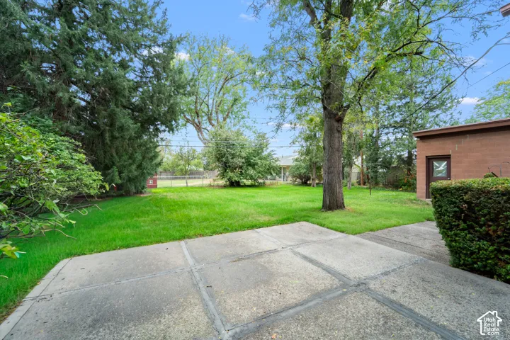 Backyard featuring a concrete patio, expansive lawn, mature trees, and masonry exterior walls