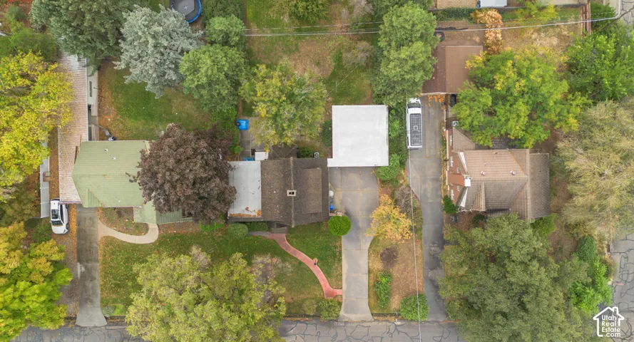 Aerial perspective of residential property featuring a paved driveway, multiple mature trees, and established landscaping