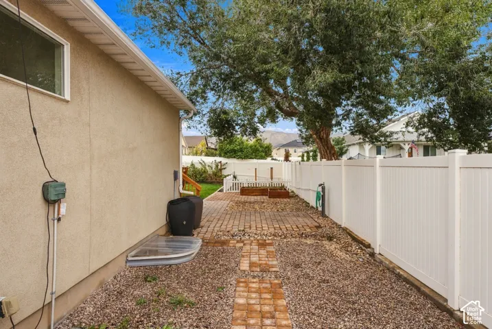 Side yard featuring a paver walkway, gravel landscaping, a white vinyl privacy fence, and mature tree canopy