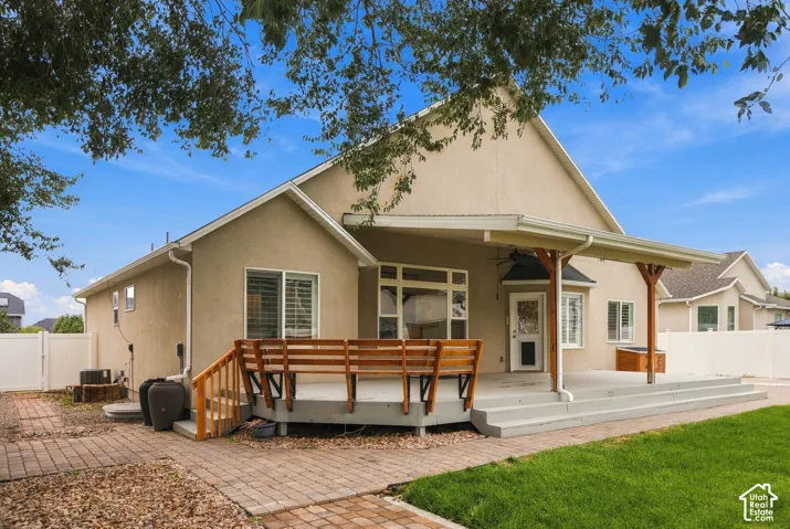 Stucco exterior featuring a covered patio, multi-level wood deck, paver stone walkway, and manicured lawn