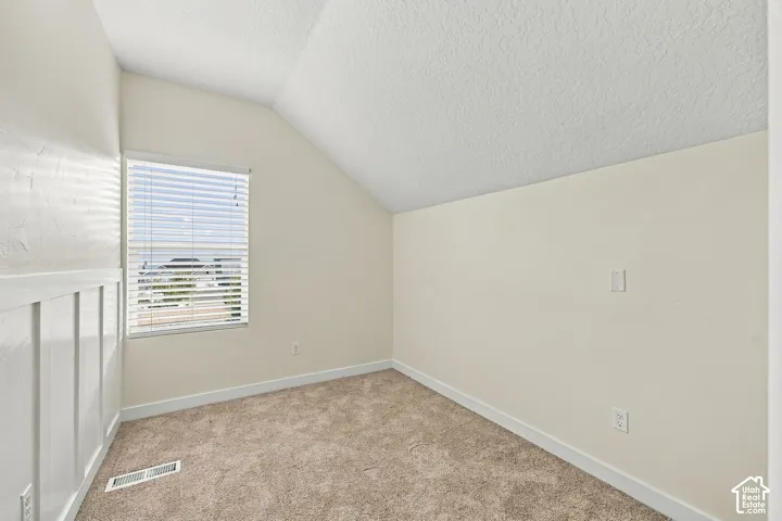 Room featuring a vaulted ceiling, neutral wall-to-wall carpeting, and white wainscoting