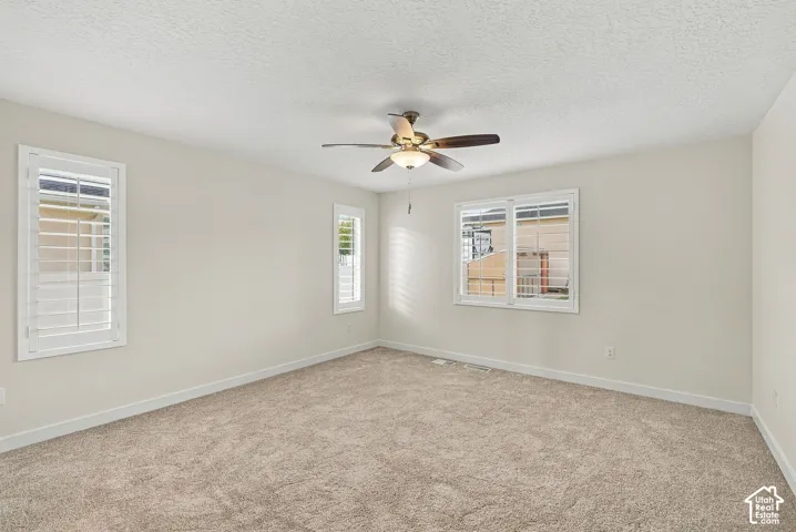 Neutral-toned room featuring neutral wall-to-wall carpeting, three windows with white plantation shutters, and a central ceiling fan with an integrated light fixture