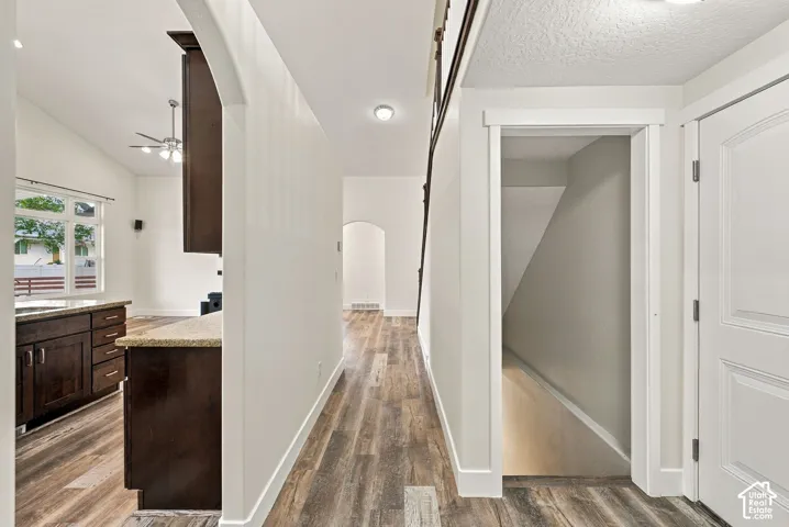 Interior hall featuring wood-finish flooring, arched doorways, dark wood cabinetry, stone countertops, and multi-panel interior doors