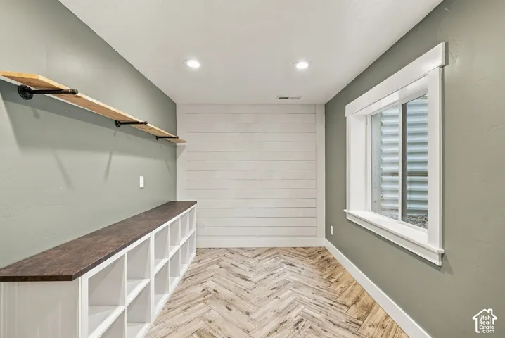 Room featuring white shiplap accent wall, herringbone wood-finish flooring, built-in lower cabinetry with dark wood-finish countertop, and industrial-style floating wall shelving