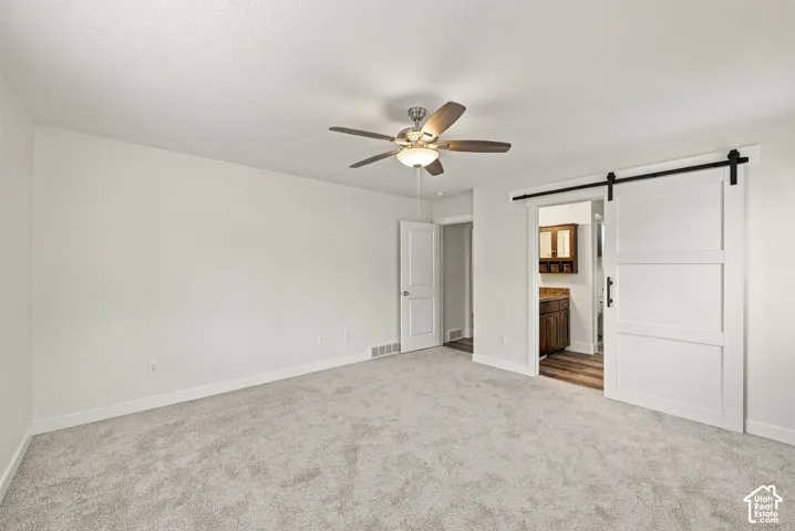 Neutral wall-to-wall carpeting, white sliding barn door with matte black hardware, and ceiling fan with integrated lighting fixture