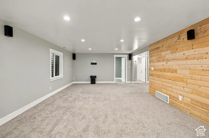 Neutral-toned interior space featuring recessed ceiling lighting, wall-mounted audio speakers, and a prominent wood-plank accent wall