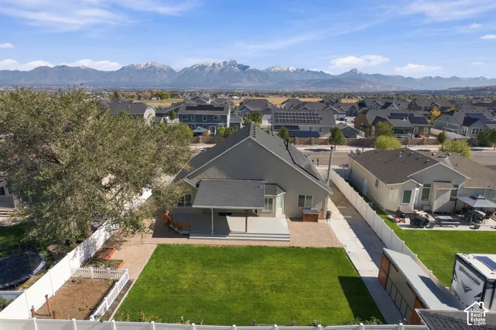 Aerial perspective featuring an expansive lawn, concrete patio, white vinyl perimeter fencing, and mountain backdrop