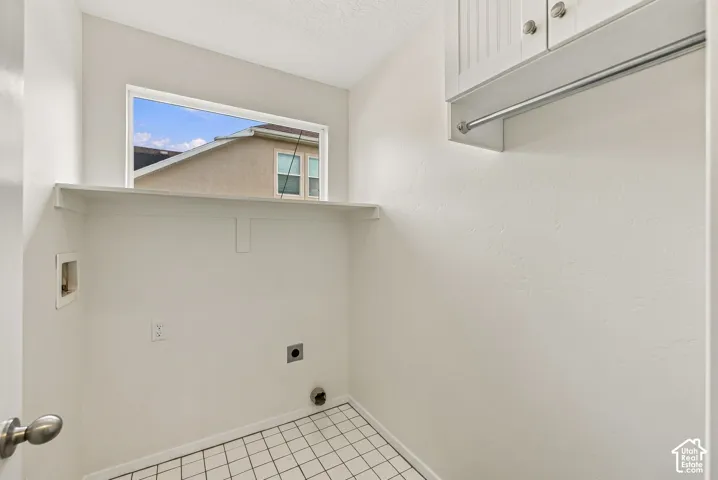 Laundry area featuring ceramic tile flooring, built-in upper cabinetry, a mounted garment rod, and a horizontal window with a continuous shelf