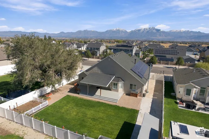 Exterior featuring a covered patio, solar panels, fenced yard with lawn and garden area, and a mountain backdrop